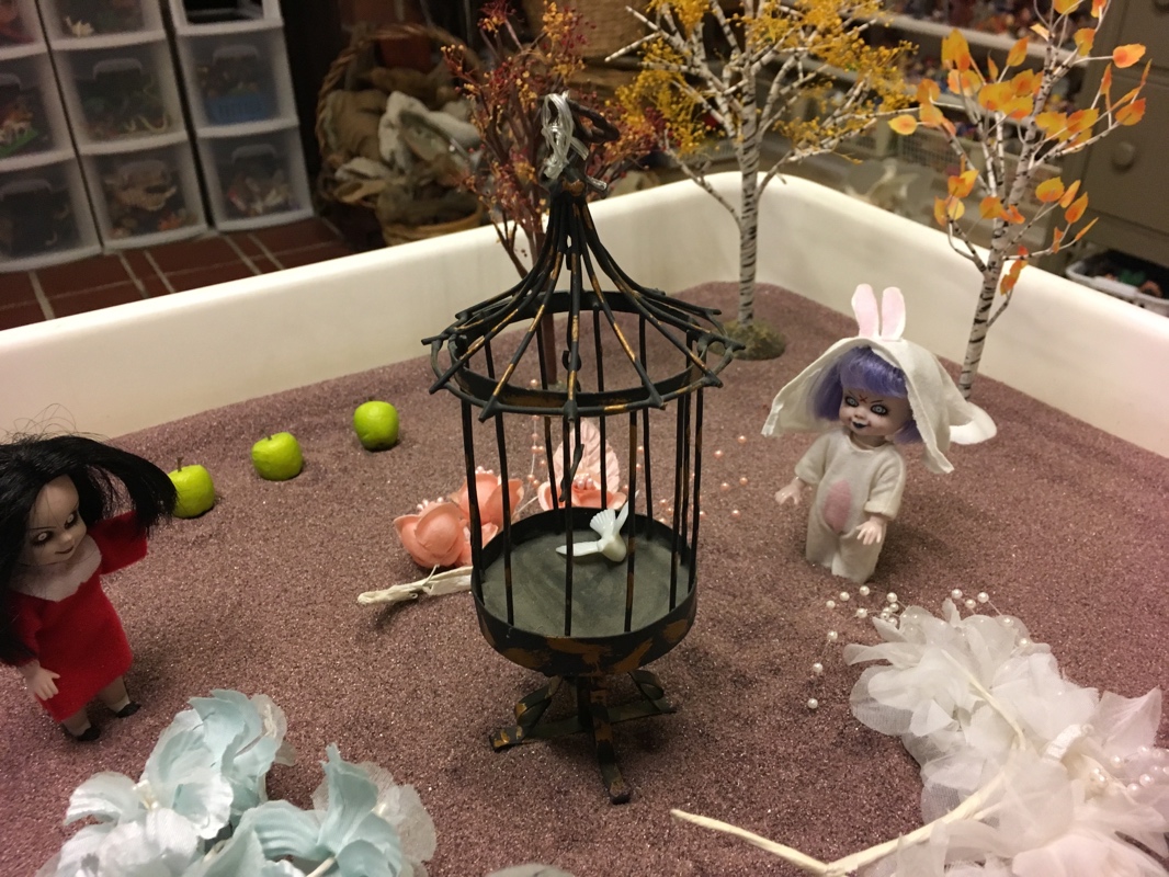 A small bird cage with flowers and toys
