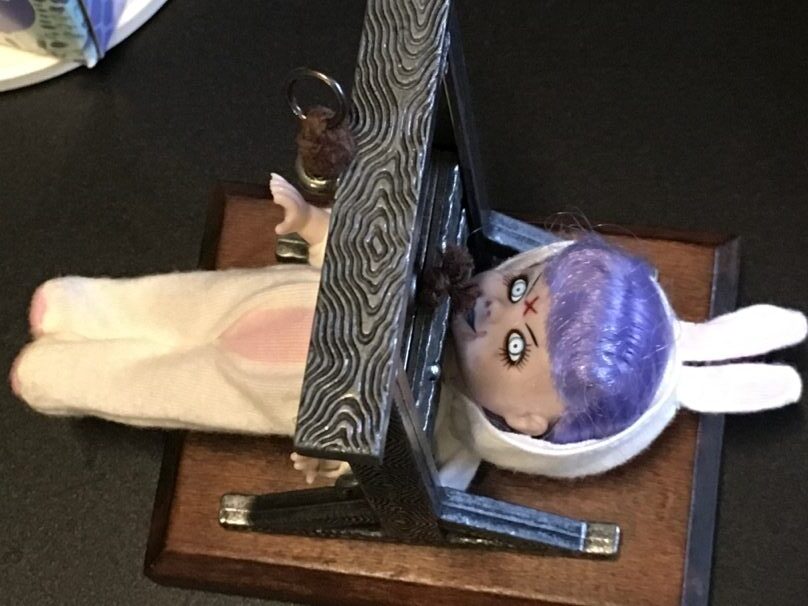 A doll with purple hair and a white bunny ears on a wooden table  Description automatically generated